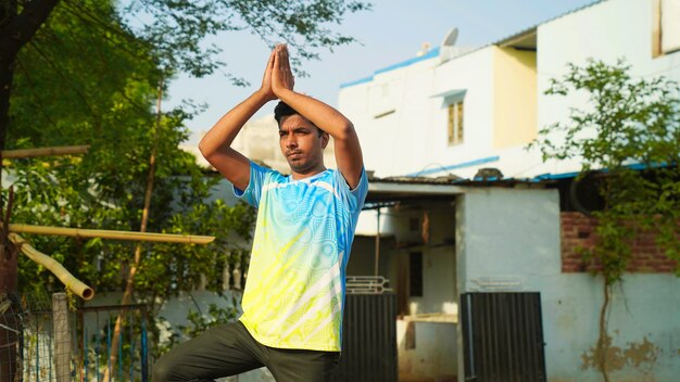 Indian man practices balance yoga asana vrikshasana tree pose at outdoor