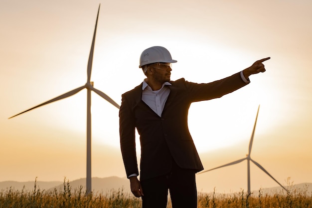 Indian man in suit keeping arms crossed among windmill farm