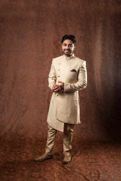 Indian man in traditional wear OR kurta, pyjama cloths.  Male fashion model in sherwani, posing or standing against brown grunge background, selective focus