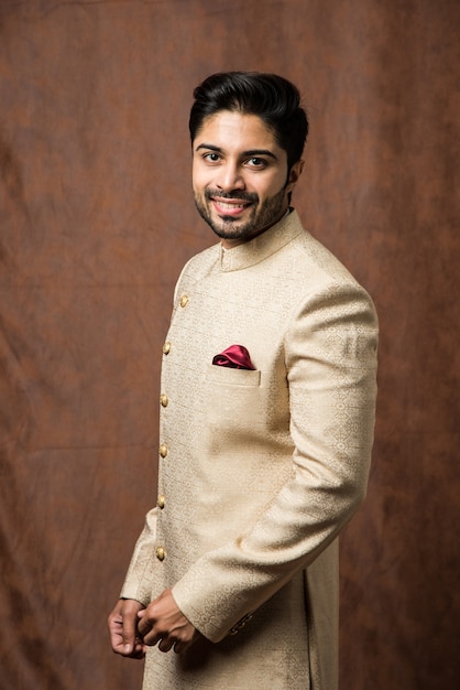 Indian man in traditional wear OR kurta, pyjama cloths.  Male fashion model in sherwani, posing or standing against brown grunge background, selective focus