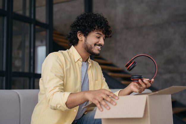 Indian man unpacking box holding headphones sitting at home Unpacking parcel delivery concept