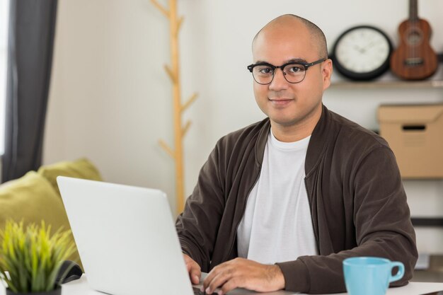 Indian man using laptop sitting in living room texting on laptop sending message