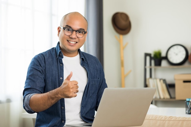 Indian man using laptop on sofa in living room texting on laptop sending message or chatting