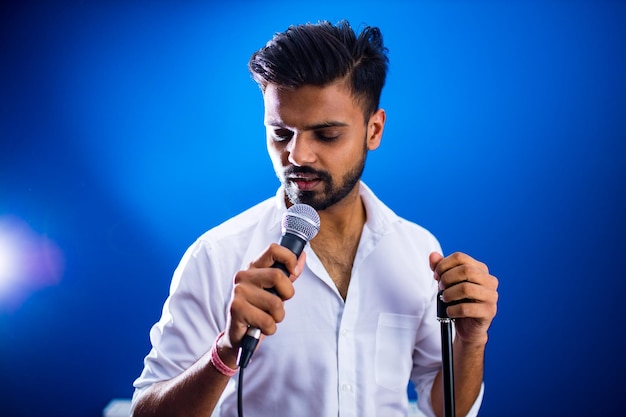 Indian man in white shirt with beard singing in recording studio on blue background