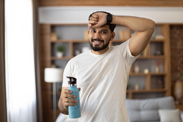 Photo indian man wiping sweat and drinking water during sport