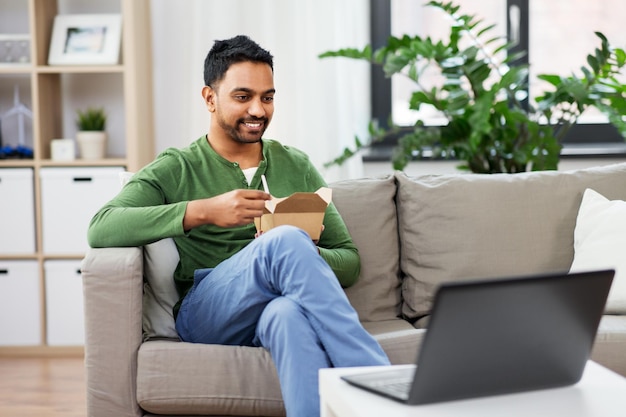 indian man with laptop eating takeout food at home