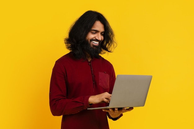 長いとひげのインド人男性はラップトップコンピュータの使用に集中しながら座っています彼のは