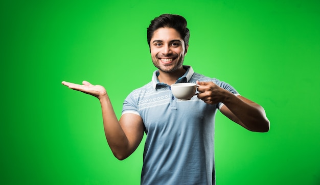 Indian man with tea or coffee cup or mug. Drinking, presenting or holding while standing isolated