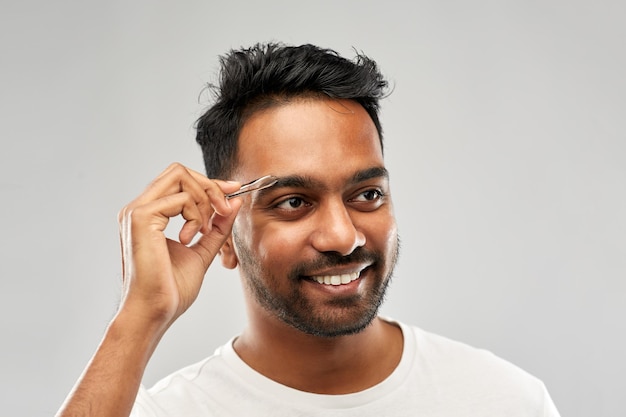 indian man with tweezers tweezing eyebrow hair