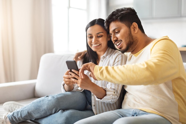 Indian man and woman sitting on couch looking at cell phone