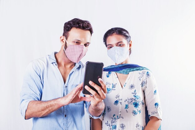 Indian man and woman wearing face masks and using mobile phone