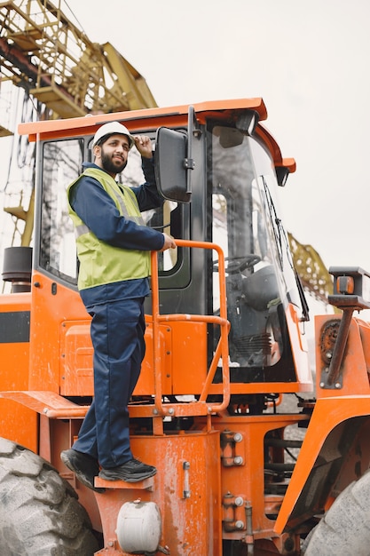 Indian man working. Male in a yellow vest. Man near the tractor.