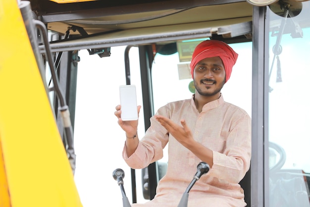 Indian man working with heavy earth moving machinery and showing smartphone screen.