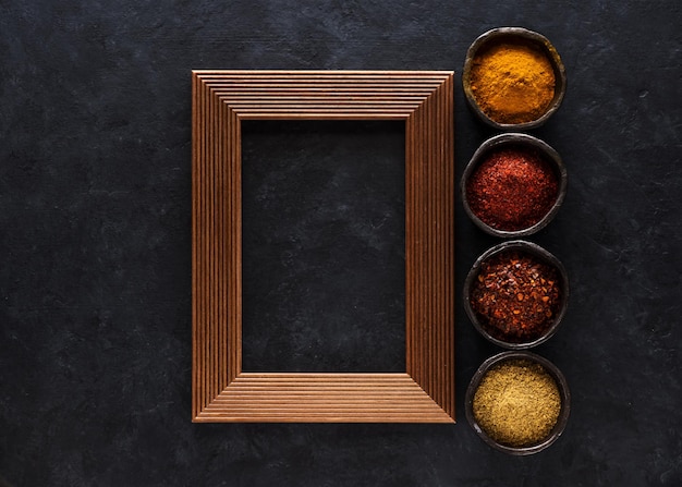 Indian masala spices and herbs in bowls and empty wooden frame for text
