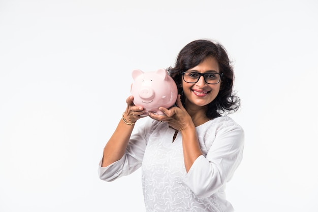 Indian mid age lady or women with piggy bank, standing isolated over white background