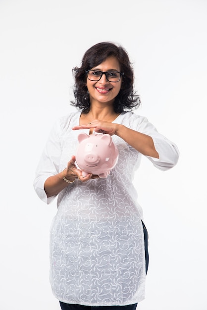 Indian mid age lady or women with piggy bank, standing isolated over white background