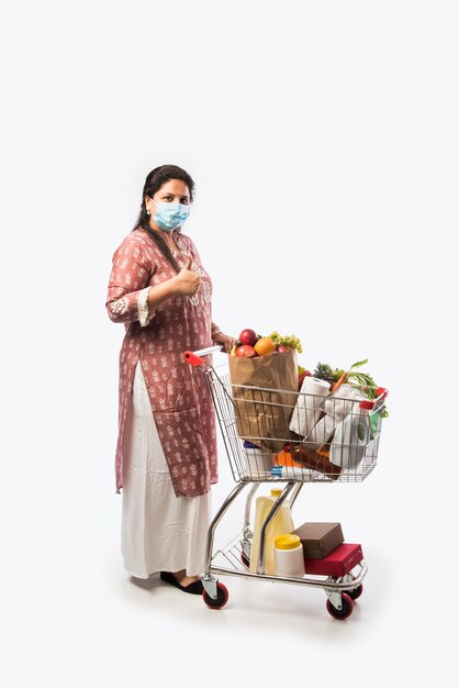 Indian mid age woman with shopping cart or trolly full of grocery vegetables and fruits  Isolated Full length photo over white background