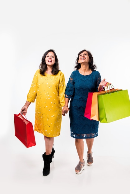 Indian Mother daughter sisters shopping with colourful bags, standing isolated over white background