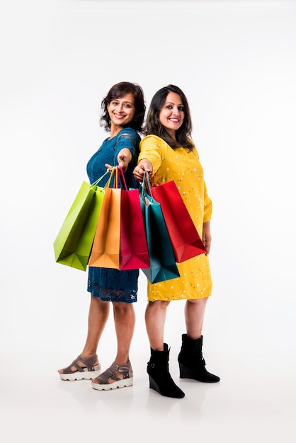 Indian Mother daughter sisters shopping with colourful bags, standing isolated over white background