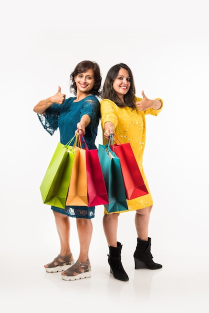 Indian Mother daughter sisters shopping with colourful bags, standing isolated over white background