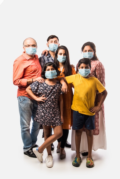 Многопоколенная индийская семья носит защитную медицинскую маску для лица во время вспышки коронавируса и гриппа. изолированные над белой стеной