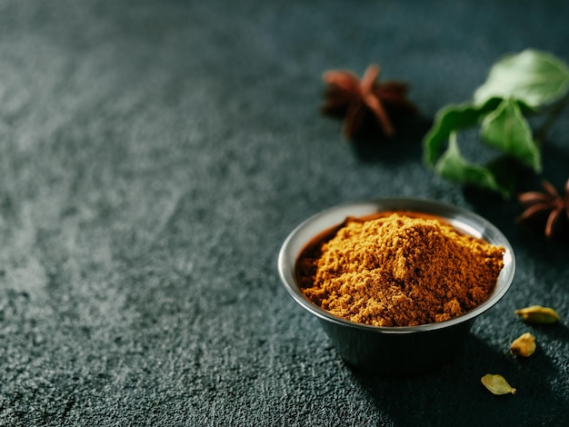 Photo indian or pakistani masala powder and spices on dark textured background small metall bowl with dry curry garam masala mix spices blend green bay leaf cardamom and star anise with copy space left