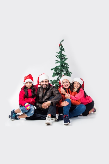 Indian people celebrating Christmas in warm clothes with tree in the white background