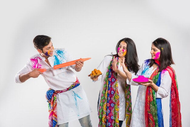 Indian people celebrating holi with sweet laddu, colours in thali and colour splash