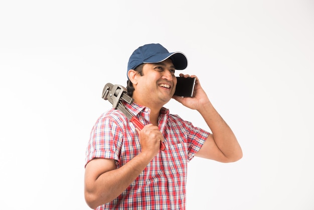Indian plumber holding drawing roll and Pipe wrench or plumbing spanner or smartphone, standing isolated