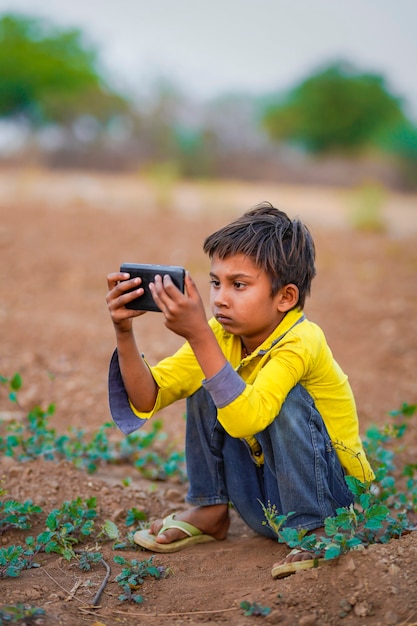 Indian poor child playing with mobile at agriculture field. Rural scene.