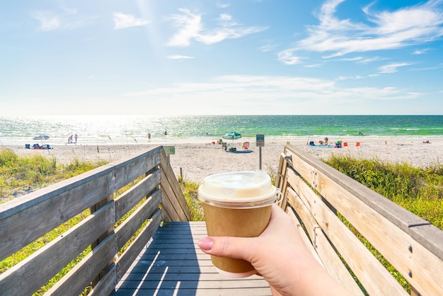 Indian rocks beach in Florida USA with Hand holding paper cup of hot coffee