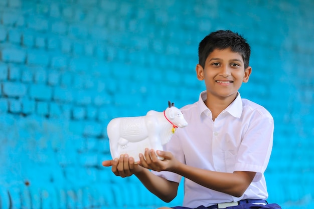 Indian school boy holding cow shape piggy bank in hand