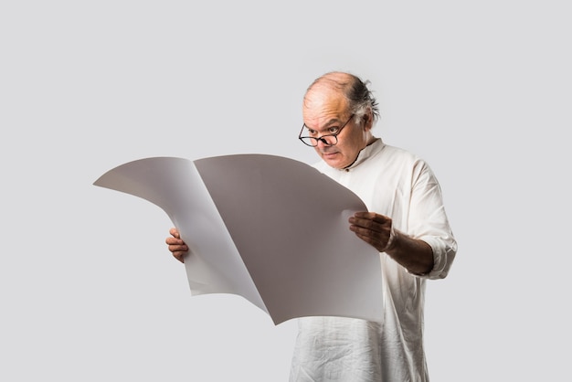 Indian senior adult man reading book or newspaper - hobby or leisure concept