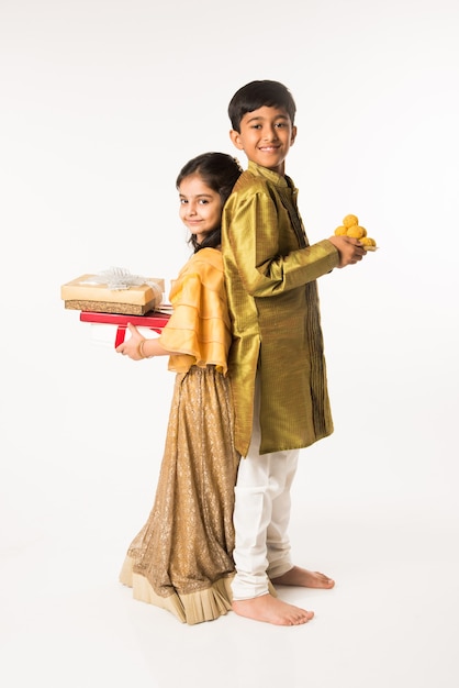 Indian small brother and sister in traditional wear standing with sweet laddu and gift boxes