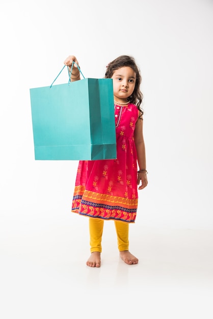 Indian small girl holding shopping bags, standing isolated over white background