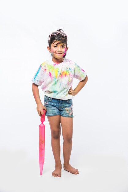 Indian small kids or friends or siblings celebrating Holi festival with gulal or powder colour, sweets, pichkari or spray, isolated over white background