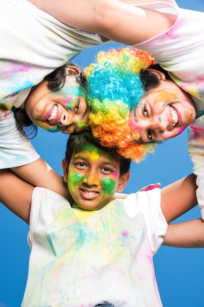 Indian small kids or friends or siblings celebrating Holi festival with gulal or powder colour, sweets, pichkari or spray, isolated over white background