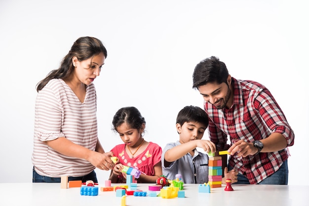 Indian small kids playing colourful block toys with young parents, against white background