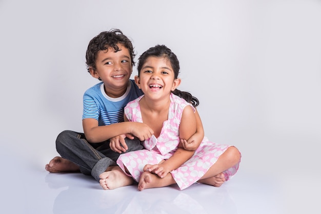 Indian small siblings hugging, portrait of 2 indian kids, Indian small boy and small girl sitting close together over white background, cheerful indian boy and girl posing for a photo