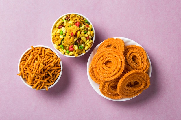 Photo indian snack : chakli, chakali or murukku and besan (gram flour) sev and chivada or chiwada on pink surface. diwali food