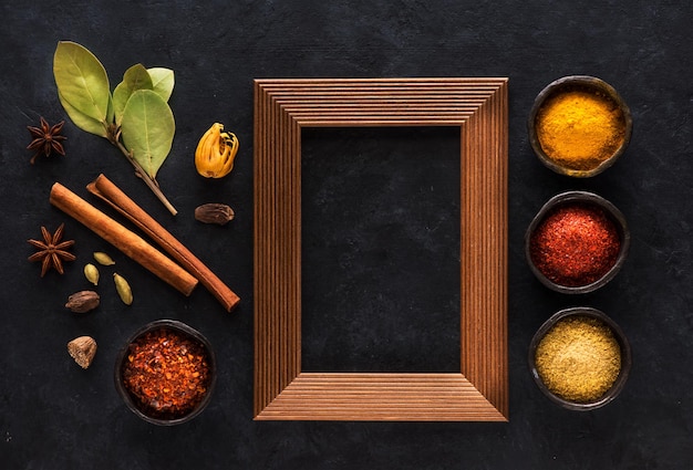 Indian spices and empty wooden frame for text on black concrete background top view flat lay