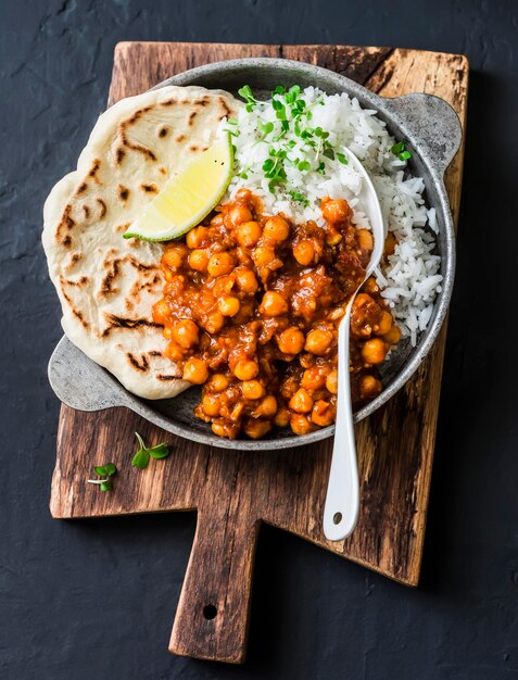 Indian spicy chickpeas curry with rice and naan bread in pan on dark background top view