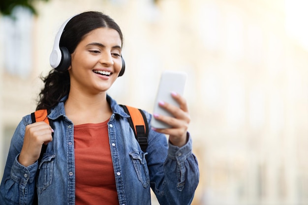 Indian student smiling with headphones using phone