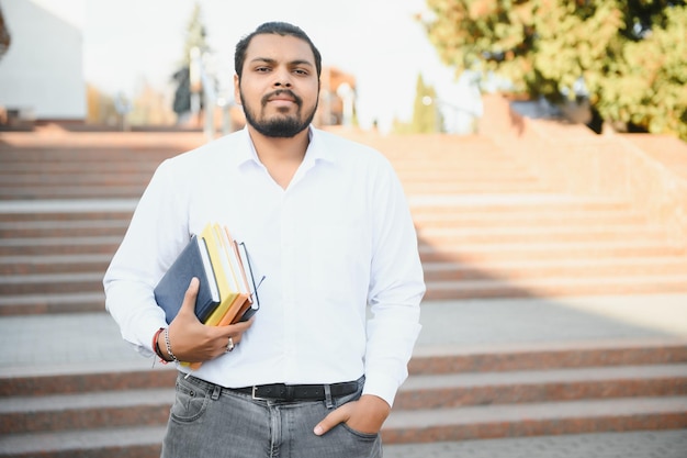 Indian student with backpack holding books at sunny day