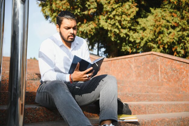 Indian student with backpack holding books at sunny day