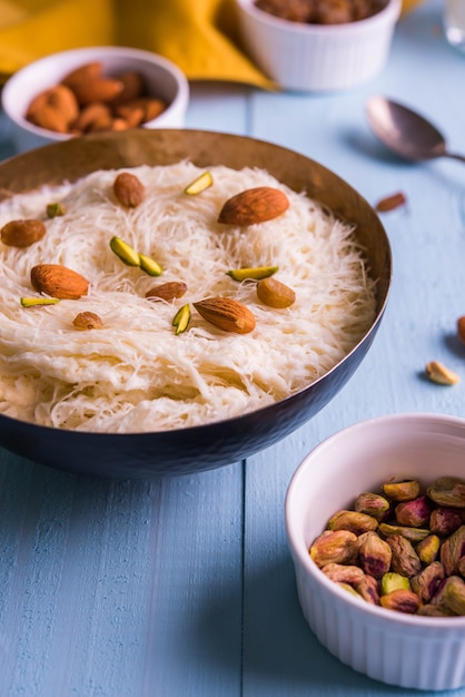 Indian sweet sutarfeni or sutar feni or firni or seviyan or laccha, shredded, flaky-rice-flour roasted in ghee, blended with melted sugar to form a cotton candy, topped with pistachio and almonds