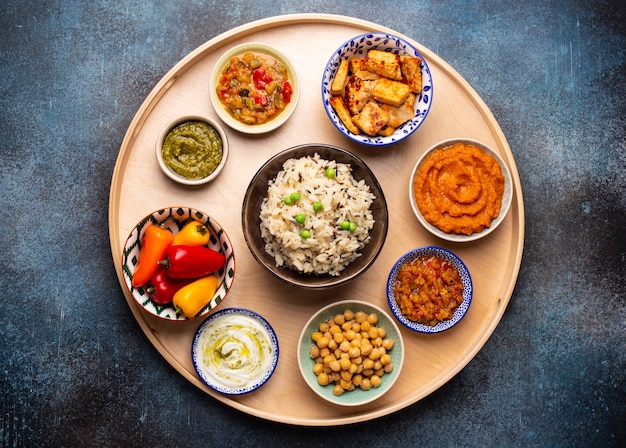 Indian Thali - selection of various dishes served on round wooden platter. Assorted Indian vegetarian meze with boiled basmati rice, paneer, dal, chutney in different bowls. Top view