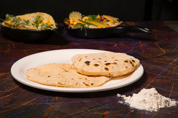 インドの伝統料理チャパティまたはロティ、またはインドのパンを白い皿に小麦粉を添えて