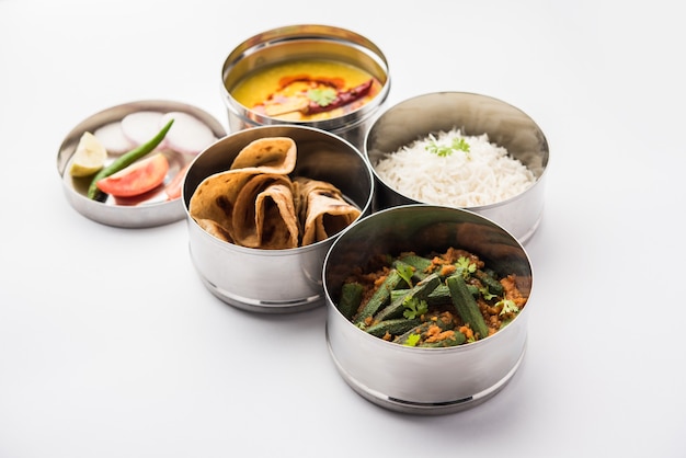 Indian vegetarian Lunch Box or Tiffin made up of stainless steel for office or workplace, includes Dal Fry, Bhindi Masala, Rice with chapati and salad