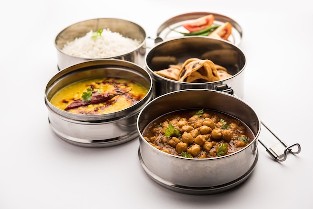 Photo indian vegetarian lunch box or tiffin made up of stainless steel for office or workplace, includes dal fry, chole masala, rice with chapati and salad